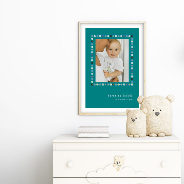 viser rektangulaer fødselstavle med et foto omkranset af en soed kant af blomster i blaa farver. Dertil fornavn og foedselsdata. Teal baggrund og hvid kant. Designet af www.plakatcompagniet.dk. plakat haenger paa boernevaerelse over hvid kommode