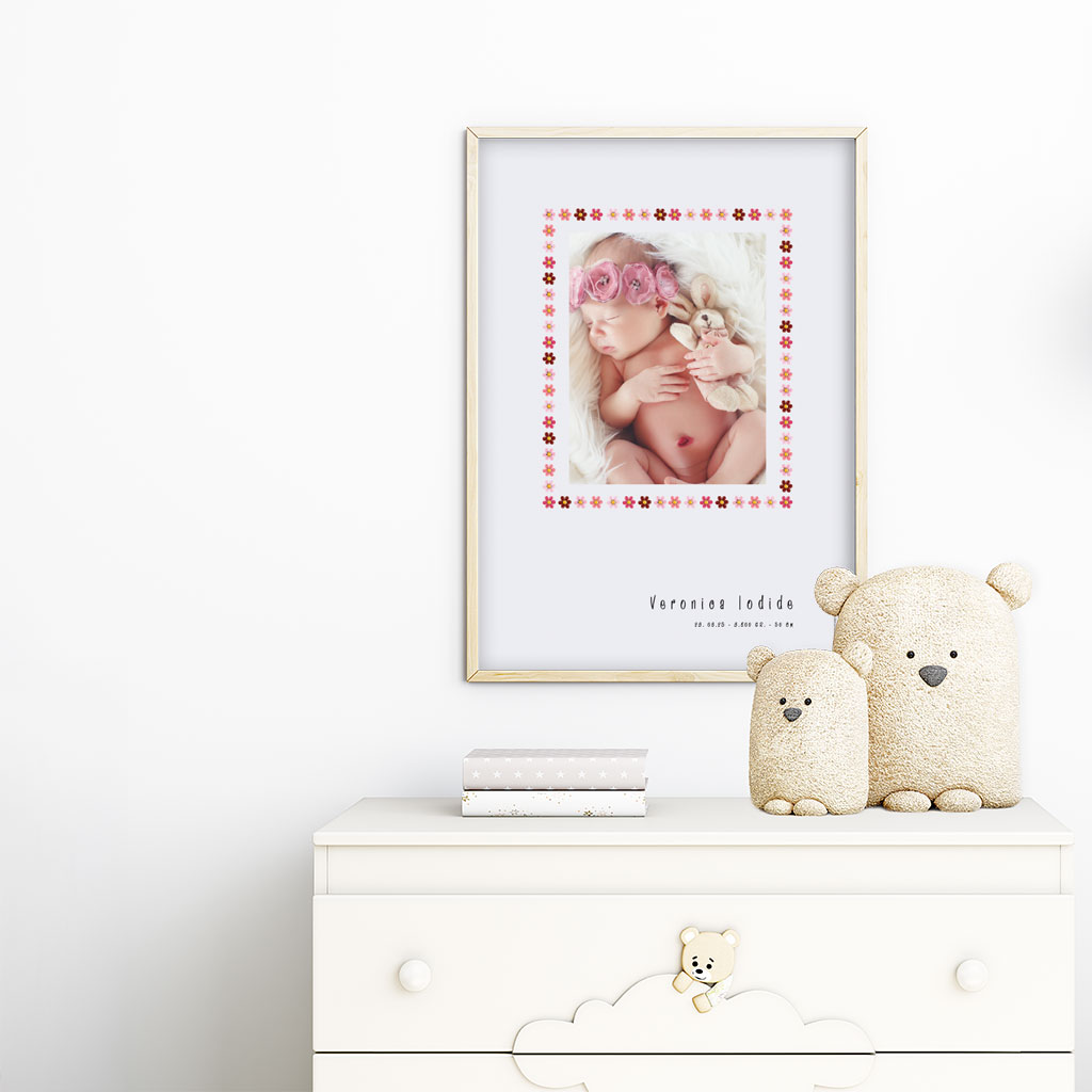 viser rektangulaer fødselstavle med et foto omkranset af en soed kant af blomster i rosa farver. Dertil fornavn og foedselsdata. Graa baggrund. Designet af www.plakatcompagniet.dk x