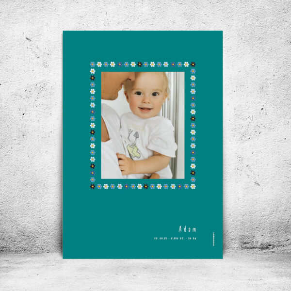 viser rektangulaer fødselstavle med et foto omkranset af en soed kant af blomster i blaa farver. Dertil fornavn og foedselsdata. Teal baggrund. Designet af www.plakatcompagniet.dk