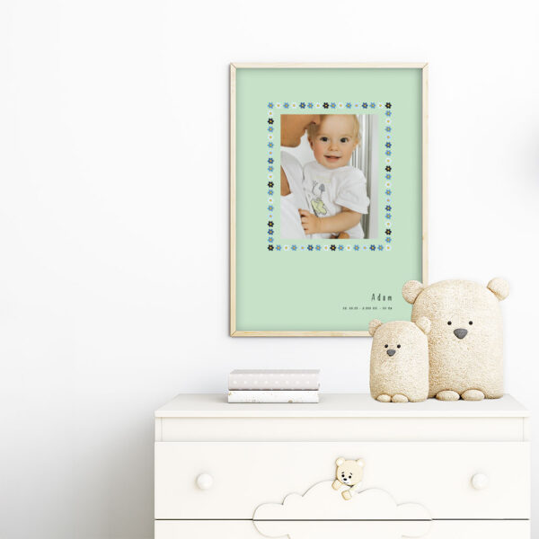 viser rektangulaer fødselstavle med et foto omkranset af en soed kant af blomster i blaa farver. Dertil fornavn og foedselsdata. Mint baggrund. Designet af www.plakatcompagniet.dk. plakat haenger paa boernevaerelse over hvid kommode