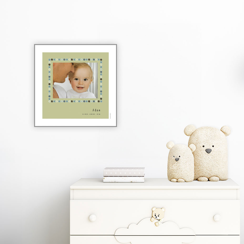 viser kvadratisk fødselstavle med et foto omkranset af en soed kant af blomster i blaa farver. Dertil fornavn og foedselsdata. Groen baggrund og hvid kant. Designet af www.plakatcompagniet.dk. plakat haenger paa boernevaerelse over hvid kommode